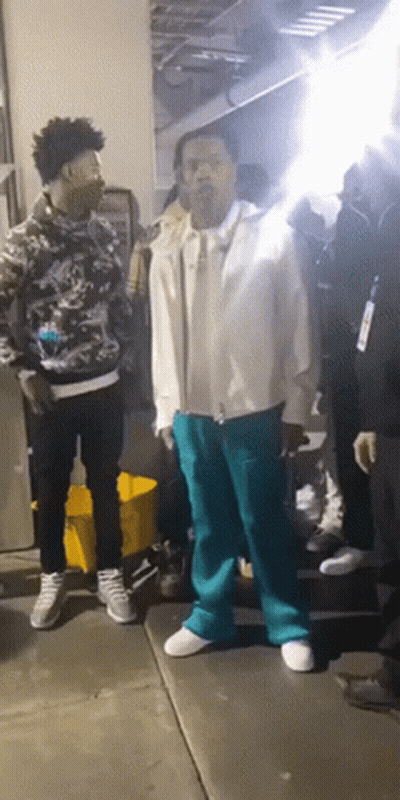 A Man In A White Jacket And Blue Pants Is Standing In A Crowd Of People GIF
