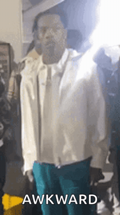 A Man In A White Jacket And Blue Pants Is Standing In Front Of A Crowd With The Word Awkward On The Bottom . GIF