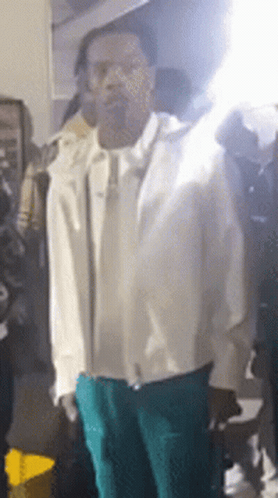 A Man In A White Jacket And Green Pants Is Standing In Front Of A Crowd Of People . GIF