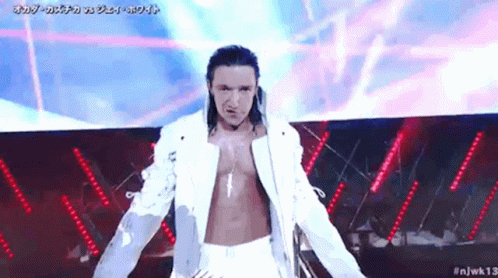 A Man In A White Jacket And White Pants Is Standing On A Stage With His Arms Outstretched . GIF