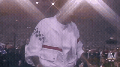 A Man In A White Jacket Is Dancing On Stage In Front Of A Crowd . GIF