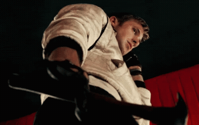 A Man In A White Jacket Is Holding A Hammer In Front Of A Red Curtain GIF