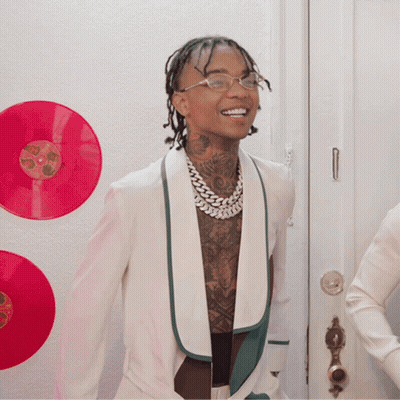 A Man In A White Jacket Is Smiling In Front Of A Wall With Red Records GIF