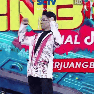 A Man In A White Jacket Is Standing In Front Of A Large Sign That Says ' Sctv ' On It . GIF