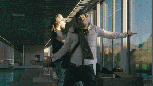 A Man In A White Jacket Is Standing In Front Of A Large Window GIF
