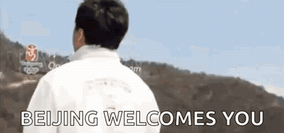 A Man In A White Jacket Is Standing In Front Of A Sign That Says Beijing Welcomes You . GIF