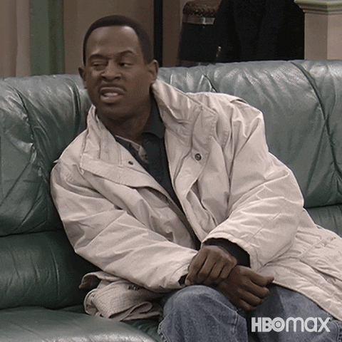 A Man In A White Jacket Sits On A Couch With Hbomax Written On The Bottom Right GIF