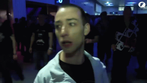 A Man In A White Jacket Stands In A Crowd Of People With The Letter F In The Corner GIF