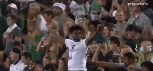 A Man In A White Jersey Is Standing In Front Of A Crowd . GIF
