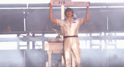 A Man In A White Jumpsuit Is Holding Up A Sign That Says ' I Love You ' On It GIF