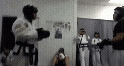 A Man In A White Karate Uniform Is Fighting Another Man In A Black Belt In A Room . GIF