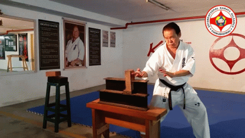 A Man In A White Karate Uniform Is Standing In Front Of A Sign That Says Dojo Oliver GIF