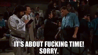 A Man In A White Karate Uniform Is Talking To A Man In A Black Belt In A Crowd Of People . GIF