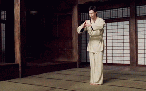 A Man In A White Karate Uniform Stands In A Room With Sliding Glass Doors GIF