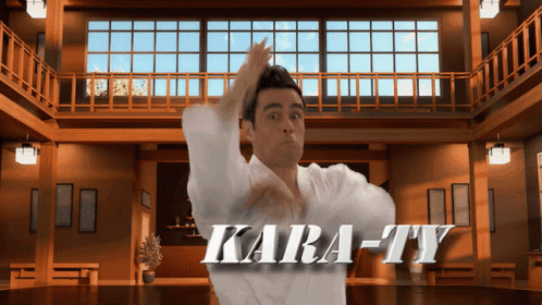 A Man In A White Karate Uniform Stands In Front Of A Sign That Reads Kara-Ty GIF