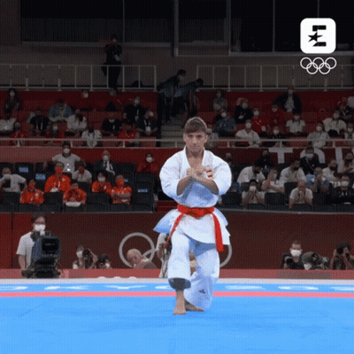 A Man In A White Karate Uniform With A Red Belt Performs A Karate Move In Front Of A Crowd At The Olympics GIF