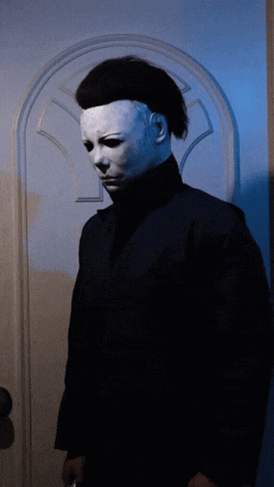 A Man In A White Mask Stands In Front Of A Blue Door GIF