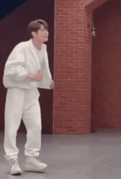 A Man In A White Outfit Is Dancing In Front Of A Brick Wall . GIF
