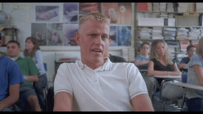 A Man In A White Polo Shirt Sits At A Desk In A Classroom GIF