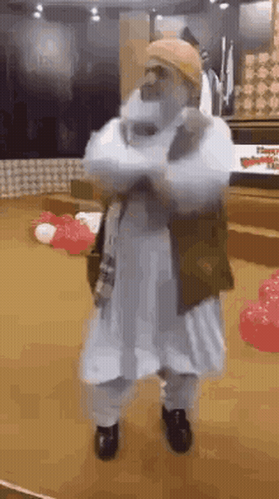 A Man In A White Robe And Hat Is Dancing In A Room . GIF