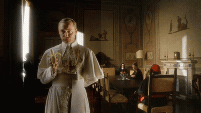 A Man In A White Robe Holds A Banana In A Room GIF