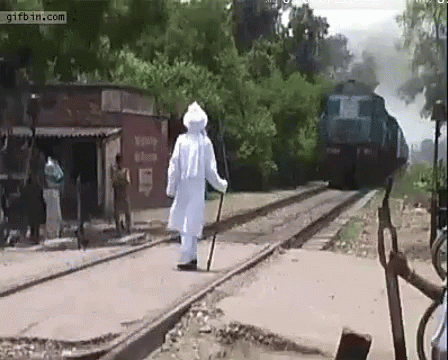 A Man In A White Robe Is Crossing A Train Track With A Cane .. GIF
