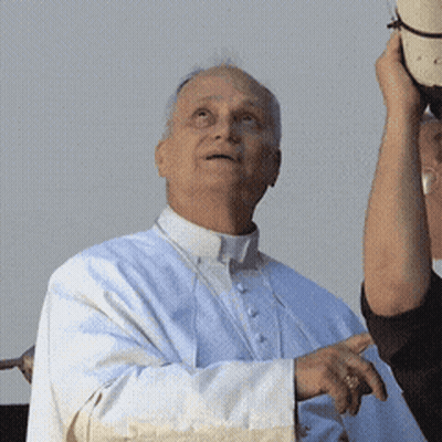 A Man In A White Robe Is Holding A Hat In His Hand GIF