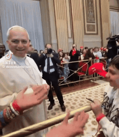 A Man In A White Robe Is Shaking Hands With A Boy In A Red Hat In Front Of A Crowd . GIF
