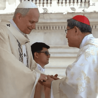 A Man In A White Robe Is Shaking Hands With A Man Wearing A Red Hat GIF
