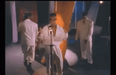 A Man In A White Robe Is Singing Into A Microphone While Standing Next To Two Other Men In Suits . GIF