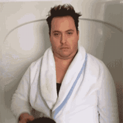 A Man In A White Robe Is Sitting In A Bathtub . GIF