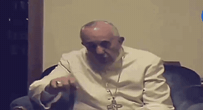 A Man In A White Robe Is Sitting In A Chair With A Cross On His Neck . GIF