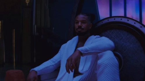A Man In A White Robe Is Sitting In A Chair With The Words Lil ' Cousin Below Him GIF