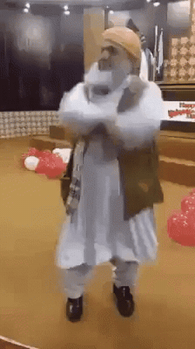 A Man In A White Robe Is Standing With His Arms Crossed In A Room With Red And White Balloons . GIF