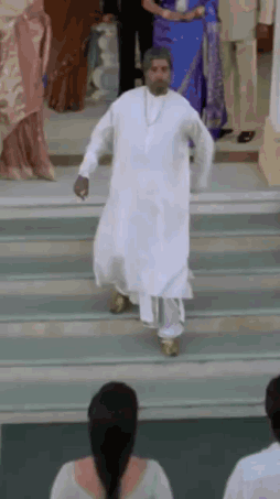 A Man In A White Robe Is Walking Down Stairs While A Woman Watches . GIF