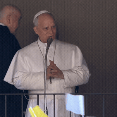 A Man In A White Robe Stands In Front Of A Microphone GIF