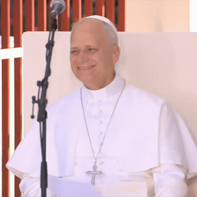 a man in a white robe stands in front of a microphone with a cross on his necklace