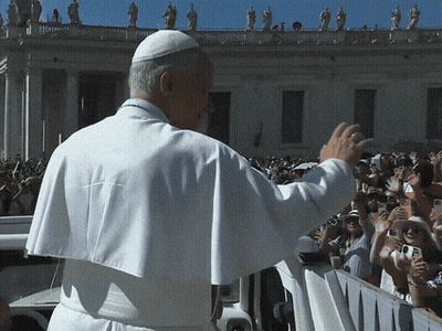 A Man In A White Robe Waves To A Crowd Of People GIF