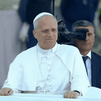 A Man In A White Robe With A Cross On His Neck GIF