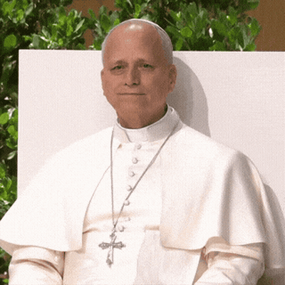 A Man In A White Robe With A Cross On His Necklace GIF