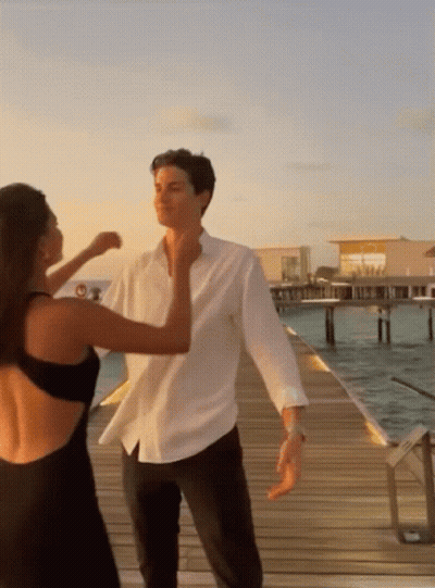 A Man In A White Shirt And A Woman In A Black Dress Are Dancing On A Dock GIF
