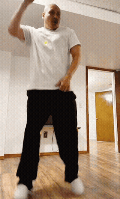 A Man In A White Shirt And Black Pants Is Dancing In An Empty Room GIF
