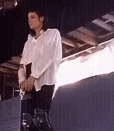 A Man In A White Shirt And Black Pants Is Sitting On A Stool . GIF