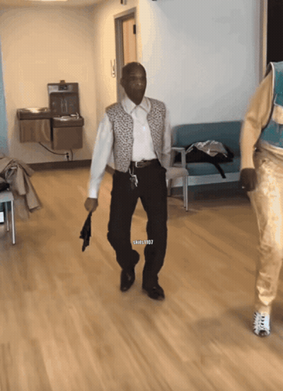 A Man In A White Shirt And Black Pants Is Walking In A Hallway With A Watermark That Says Shills1987 GIF