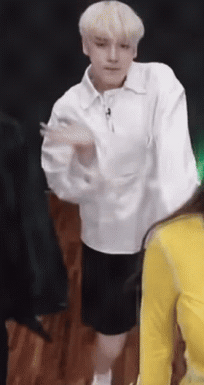 A Man In A White Shirt And Black Shorts Is Dancing In Front Of A Group Of People . GIF