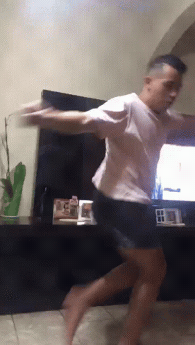 A Man In A White Shirt And Black Shorts Is Dancing In Front Of A Tv GIF