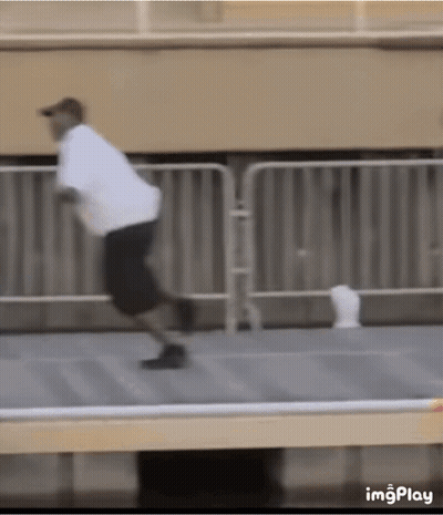 A Man In A White Shirt And Black Shorts Is Running On A Sidewalk . GIF