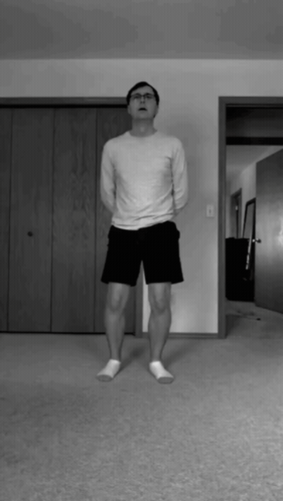 A Man In A White Shirt And Black Shorts Is Standing In A Living Room GIF