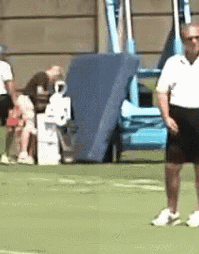 A Man In A White Shirt And Black Shorts Is Standing On A Green Field . GIF