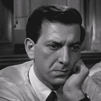 A Man In A White Shirt And Black Tie Has His Hand On His Chin GIF